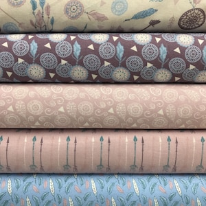 May include: A stack of fabric rolls with various patterns. The top roll features a beige background with blue and pink feathers and dream catchers. Other rolls display repeating patterns of circles, arrows, and paisley designs in shades of purple, pink, and blue.