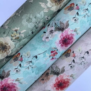 Op de afbeelding: Drie rollen stof met een bloemenprint. De stof is in tinten groen, blauw en beige met roze bloemen.