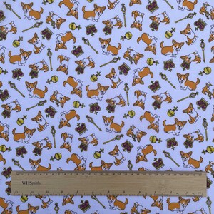 May include: White fabric with a repeating pattern of cartoon corgis wearing crowns, holding scepters, and playing with balls. The fabric is also decorated with gold keys and crowns.