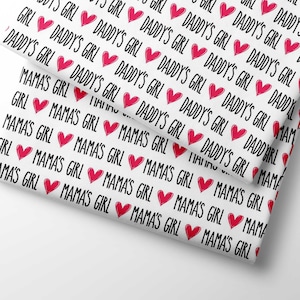 Op de afbeelding: Witte stof met een herhalend patroon van roze harten en de tekst "Mama's Girl" en "Daddy's Girl".