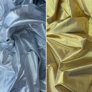 May include: Two pieces of iridescent fabric, one silver and one gold, are draped and folded. The fabric has a subtle sheen and a smooth texture.