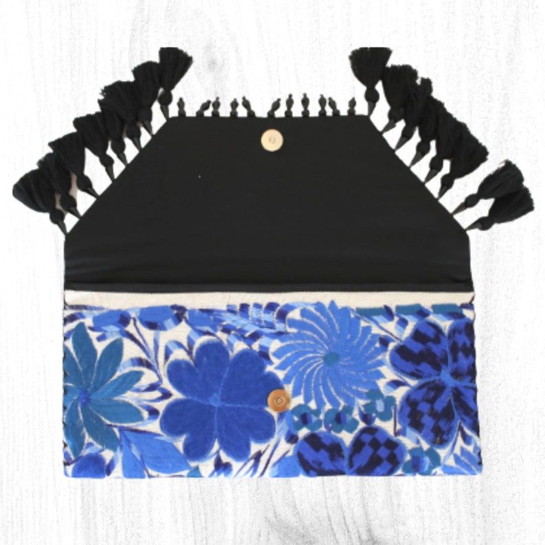 May include: A blue and white floral embroidered clutch with black tassels. The clutch has a black fabric lining and a gold button closure.