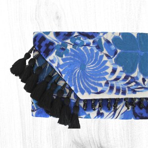 May include: A blue and white embroidered clutch bag with black tassels and black beads. The bag has a floral design.