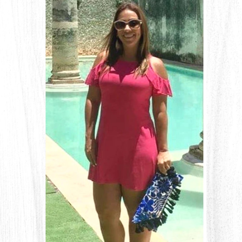 May include: A woman wearing a pink off-the-shoulder dress and sunglasses is holding a blue and white clutch with tassels.