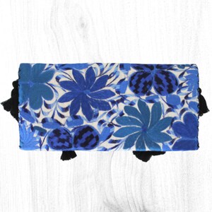 May include: A blue and white embroidered clutch with black tassels. The clutch features a floral pattern with blue and white flowers.