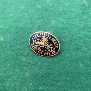 May include: A gold and black enamel pin with the text "AT&T Pebble Beach National Pro-Am".