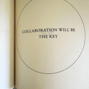 May include: Open book page with the text "COLLABORATION WILL BE THE KEY" inside a black circle. The text is in a serif font and is centered on the page. The page is a light beige color.