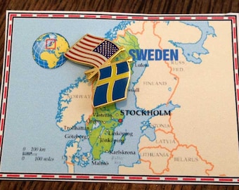 May include: A map of Sweden with a gold pin featuring the American and Swedish flags. The map shows major cities including Stockholm, Goteborg, and Malmo. The pin is placed on the city of Stockholm.