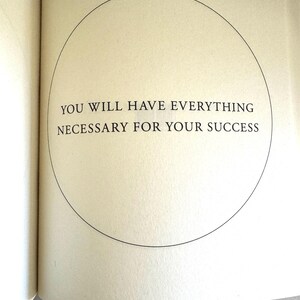 May include: Open book page with the text "YOU WILL HAVE EVERYTHING NECESSARY FOR YOUR SUCCESS" inside a black circle. The page is off-white with a slight texture. The text is in a simple, sans-serif font.