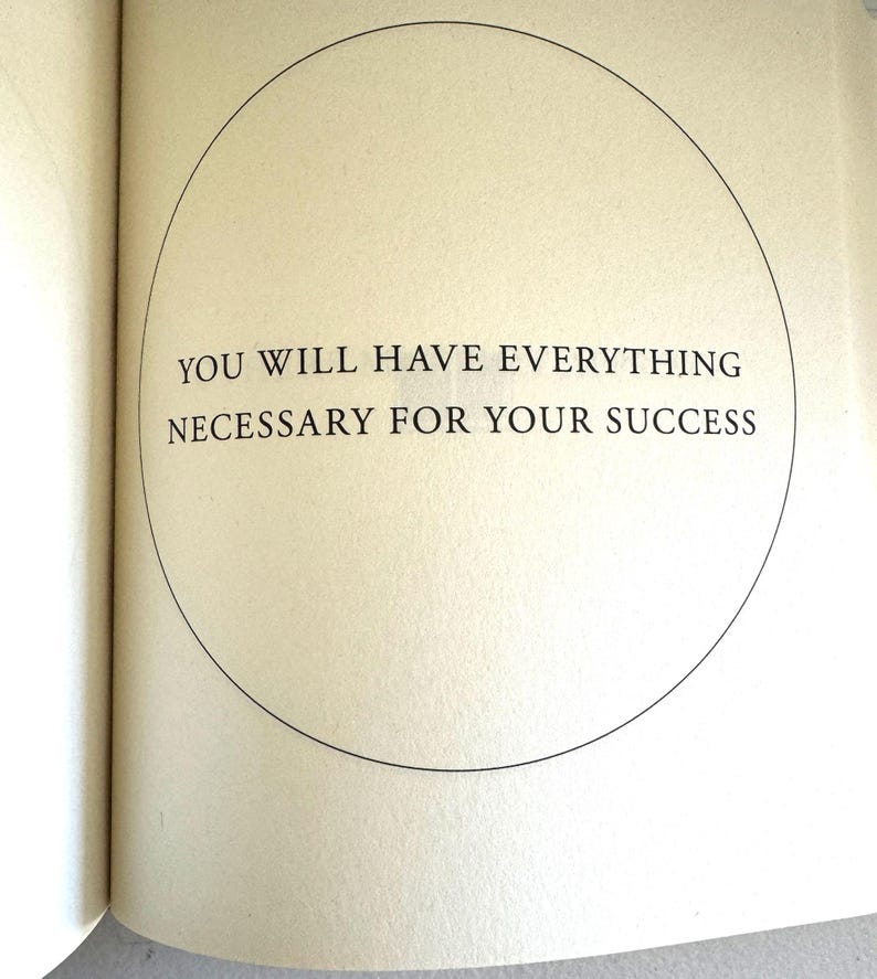 May include: Open book page with the text "YOU WILL HAVE EVERYTHING NECESSARY FOR YOUR SUCCESS" inside a black circle. The page is off-white with a slight texture. The text is in a simple, sans-serif font.