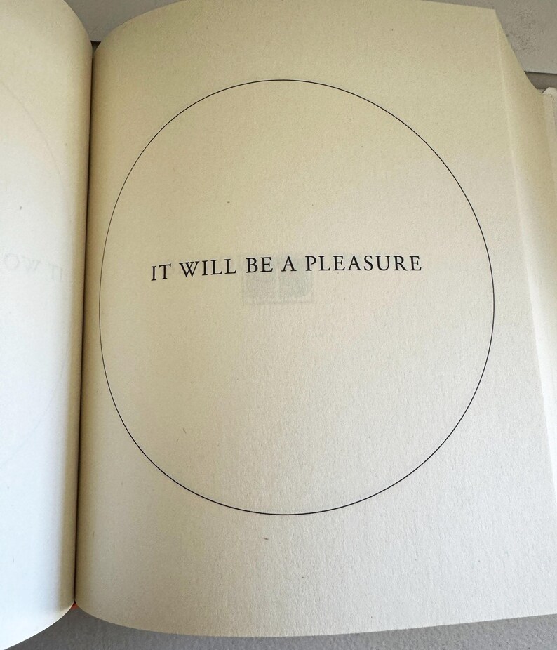 May include: Open book pages with the text "IT WILL BE A PLEASURE" inside a black circle. The text is in a serif font. The pages are off-white.