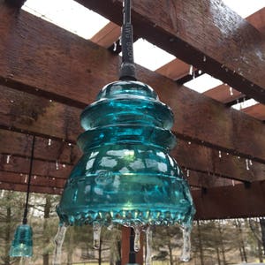 Peut inclure: Un luminaire suspendu en verre bleu turquoise avec des gla&ccedil;ons qui pendent du bas. La lumi&egrave;re est suspendue &agrave; une pergola en bois avec des gla&ccedil;ons qui pendent des poutres.