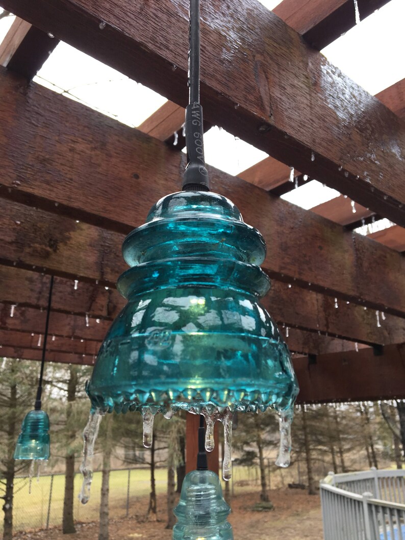 Peut inclure: Un luminaire suspendu en verre bleu turquoise avec des gla&ccedil;ons qui pendent du bas. La lumi&egrave;re est suspendue &agrave; une pergola en bois avec des gla&ccedil;ons qui pendent des poutres.