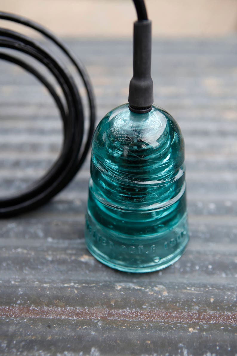 K&ouml;nnte beinhalten: Ein t&uuml;rkisfarbener Glasisolator mit einem daran befestigten schwarzen Draht. Der Isolator hat eine abgerundete Oberseite und eine zylindrische Basis. Der Draht ist um die Basis des Isolators gewickelt.