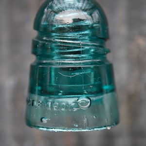 K&ouml;nnte beinhalten: Ein antiker gr&uuml;ner Glasisolatoren mit dem Datum "Oct. 13 1907" auf der Unterseite.