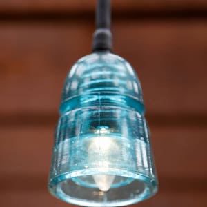 K&ouml;nnte beinhalten: Eine blaue Glaspendelleuchte mit einer klaren Gl&uuml;hbirne, die an einem schwarzen Kabel h&auml;ngt.
