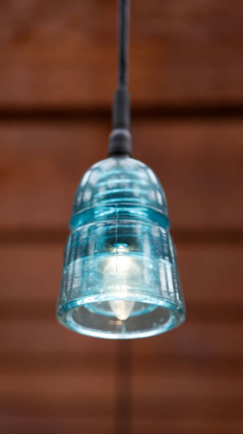 K&ouml;nnte beinhalten: Eine blaue Glaspendelleuchte mit einer klaren Gl&uuml;hbirne, die an einem schwarzen Kabel h&auml;ngt.
