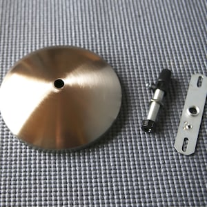 May include: A brushed nickel ceiling light fixture canopy, a threaded rod with a black plastic cap, and a metal mounting plate with two holes.