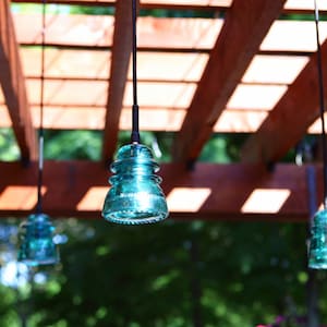 Peut inclure: Quatre lampes suspendues en verre bleu turquoise pendent d'une pergola en bois. Les lampes sont suspendues par des cordons noirs et sont nettes, tandis que l'arri&egrave;re-plan est flou.