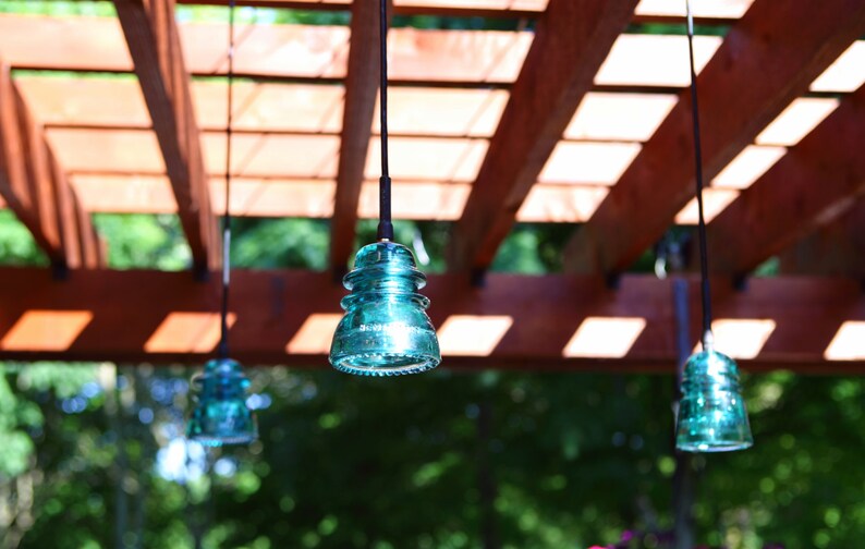 Peut inclure: Quatre lampes suspendues en verre bleu turquoise pendent d'une pergola en bois. Les lampes sont suspendues par des cordons noirs et sont nettes, tandis que l'arri&egrave;re-plan est flou.