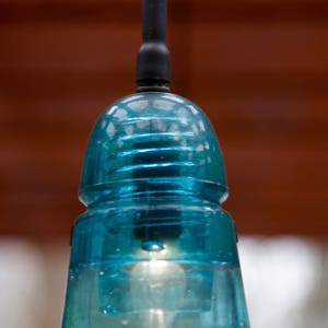 K&ouml;nnte beinhalten: Eine blaue Glaspendelleuchte mit einem schwarzen Kabel, das von einer Decke h&auml;ngt.