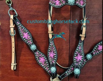 Puede incluir: Conjunto de guarnicionería de caballo de cuero negro con bordado floral rosa y detalles plateados. El conjunto incluye un cabezal, un pecho y riendas.