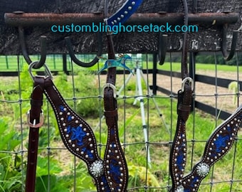 May include: A brown leather horse bridle with blue and silver embroidery and rhinestones. The bridle is hanging on a metal hook with a blue and silver studded collar.