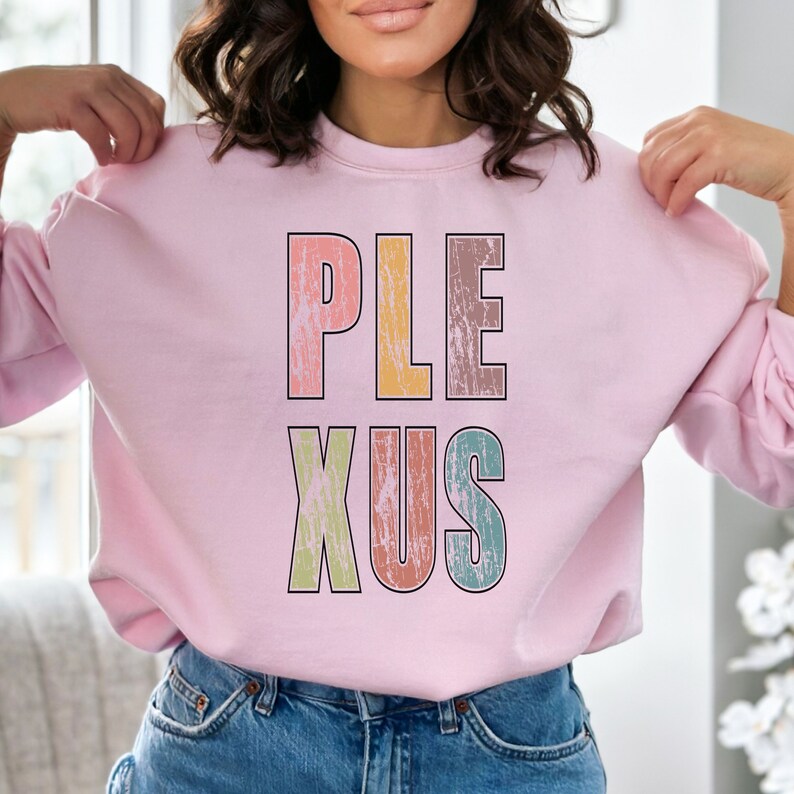 K&ouml;nnte beinhalten: Rosafarbener Pullover mit dem Wort "PLEXUS" in bunten, abgenutzten Buchstaben.