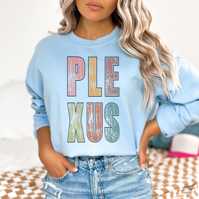 K&ouml;nnte beinhalten: Ein hellblaues Sweatshirt mit dem Wort "PLEXUS" in bunten, abgenutzten Buchstaben.