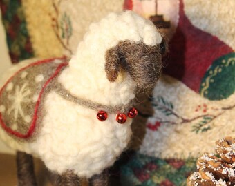 May include: A needle-felted sheep figurine with cream-colored wool, dark brown legs and face, and a gray blanket featuring a white snowflake pattern. The sheep wears a gray collar adorned with three small, shiny red jingle bells.