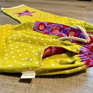 Könnte beinhalten: Gelbe Hose mit weißen Punkten und einem violetten Sternenmuster auf dem Bein. Der Bund hat ein violettes Innenfutter mit Granatapfel-Druck, einen weißen Kordelzug und ein kleines weißes Etikett mit der Aufschrift Plums and Pickles.