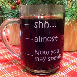 May include: A clear glass mug with a dark red liquid inside. The mug has the text "shh... almost Now you may speak" etched on the side.