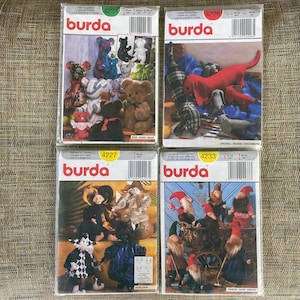 May include: Four Burda sewing pattern packets featuring various stuffed animal designs. The packets showcase patterns for bears, dachshunds, gnomes, and harlequins. Each packet has a unique product number and includes images of the finished products.