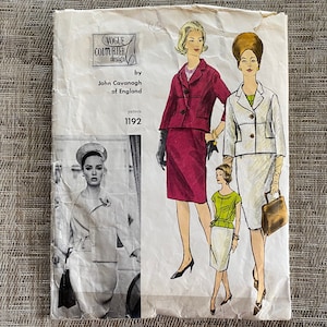 May include: A vintage Vogue Couturier Design sewing pattern envelope by John Cavanagh of England, pattern 1192. The paper envelope features illustrations of two-piece suit ensembles, including a magenta jacket and skirt, and a white jacket and skirt.