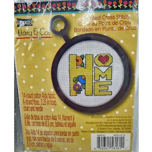 May include: A counted cross stitch kit in a yellow package with white polka dots. The kit includes 14-count Aida fabric, 6-strand floss, a 3.25 inch hoop, a chart, and a needle. The design features the word HOME in yellow with floral accents.