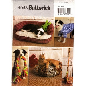 May include: A Butterick sewing pattern, number 4048, featuring various pet accessories. The image shows a dog bed, a dog wearing pajamas, a dog with a rope toy, and a cat on a leopard print bed. The pattern includes all sizes.