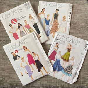 May include: Four white paper sewing pattern envelopes by McCall's, labeled 8716, M4387, M4882, and M5431. Each envelope features illustrations of various skirt styles, including midi, maxi, and A-line cuts, along with corresponding top pairings and sizing information printed on the front.