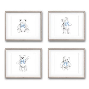 May include: Set of four framed prints featuring watercolor illustrations of white teddy bears with blue bows. Each print is in a simple gray frame.