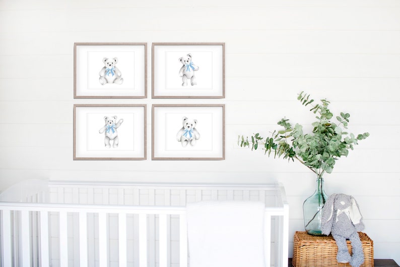 May include: Four framed prints of a white teddy bear wearing a blue bow tie. The prints are arranged in a grid on a white wall. A white crib and a vase of greenery are in the background.