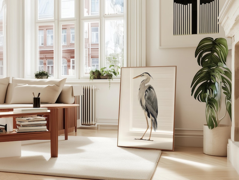 Great blue heron watercolour style illustration art print shown on a white background. The print is in a thin wood frame and is leaning against a wall in a city apartment city. Art by Nicky Quartermaine Scott for Studio Q.
