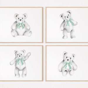 May include: Set of four framed prints featuring watercolor illustrations of teddy bears with green bows. Each print is set against a white background.