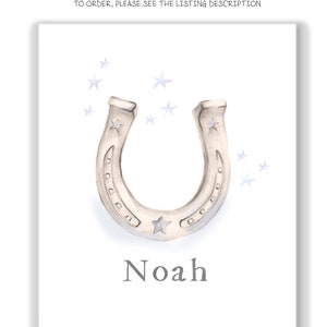 Może przedstawiać: Białe tło z srebrną podkową i jedną gwiazdą w środku. Pod podkową napisano imię "Noah". Wok&oacute;ł podkowy rozrzucone są małe niebieskie gwiazdki.