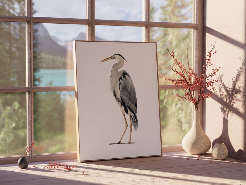 May include: A framed print of a grey heron standing on a white background. The heron is facing to the left and has a long, thin beak. The print is in a wooden frame and is hanging on a wall.