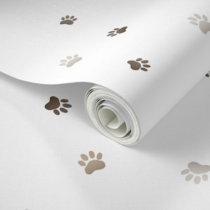 May include: White wallpaper roll with a repeating pattern of brown and tan paw prints. The paw prints are scattered across the surface, with a few prints visible on the rolled edge of the wallpaper.