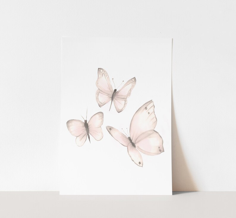 May include: Three delicate watercolor butterflies in shades of pink and gray on a white background.