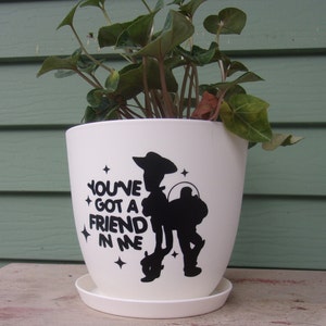 May include: White ceramic planter with a black silhouette of Woody from Toy Story and the text "You've got a friend in me".