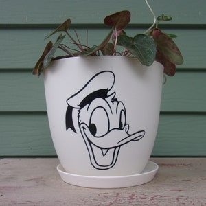 May include: White ceramic planter with a black and white cartoon image of Donald Duck. The planter has a wide rim and a saucer.