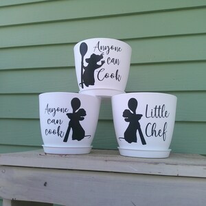 May include: Three white plastic plant pots with matching saucers, each featuring a black silhouette of a rat holding a wooden spoon. Two pots display the text "Anyone can cook" in black script, while the third pot displays "Little Chef".