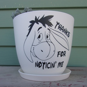 May include: White ceramic planter with a black and white illustration of Eeyore from Winnie the Pooh. The text "Thanks for Noticin' Me" is printed on the planter.