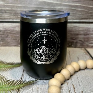 May include: Black stainless steel tumbler with a silver inscription that reads "To the stars who listen and the dreams that are answered". The inscription is surrounded by a circle with stars and a mountain range inside.